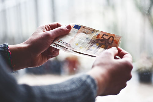 Ein Mann mit Wollpullover hält vor sich zwei 50 Euro Geldscheine