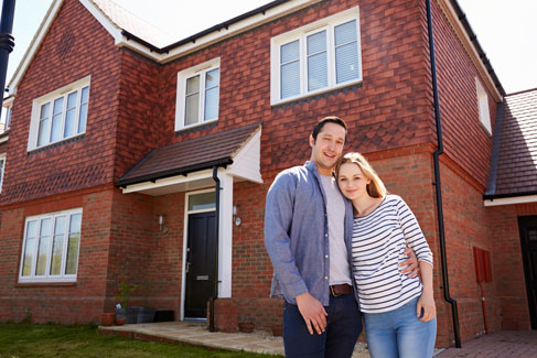 Ein junges Paar steht glücklich Arm in Arm vor seinem eigenen Haus