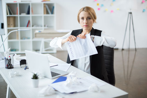Eine Geschäftsfrau sitzt am Schreibtisch und zerreißt einen Vertrag in zwei Teile